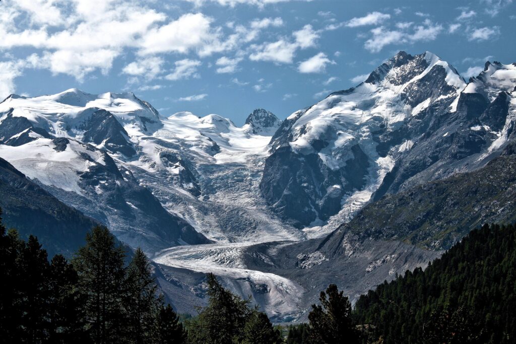 Snow-capped rugged mountains under vibrant blue sky with soft clouds serene landscape wallpaper