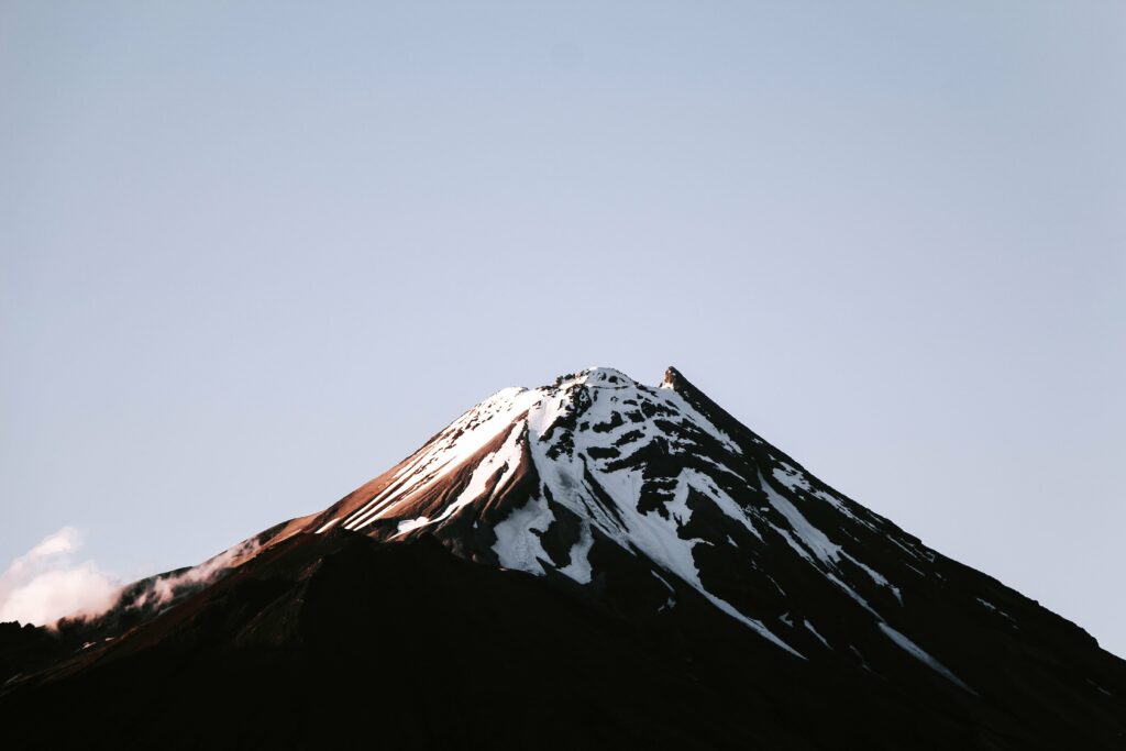 Volcanic mountain peak with snow patches under soft natural light and clear blue sky wallpaper