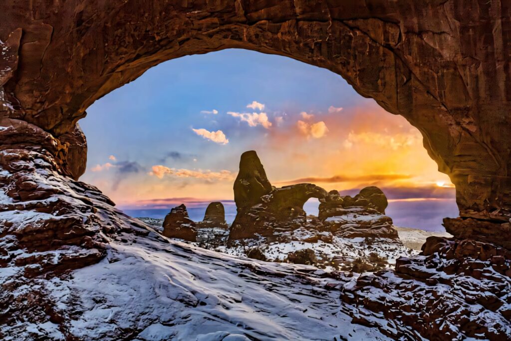Snow-covered Delicate Arch glowing in golden sunlight against vibrant winter sky landscape wallpaper