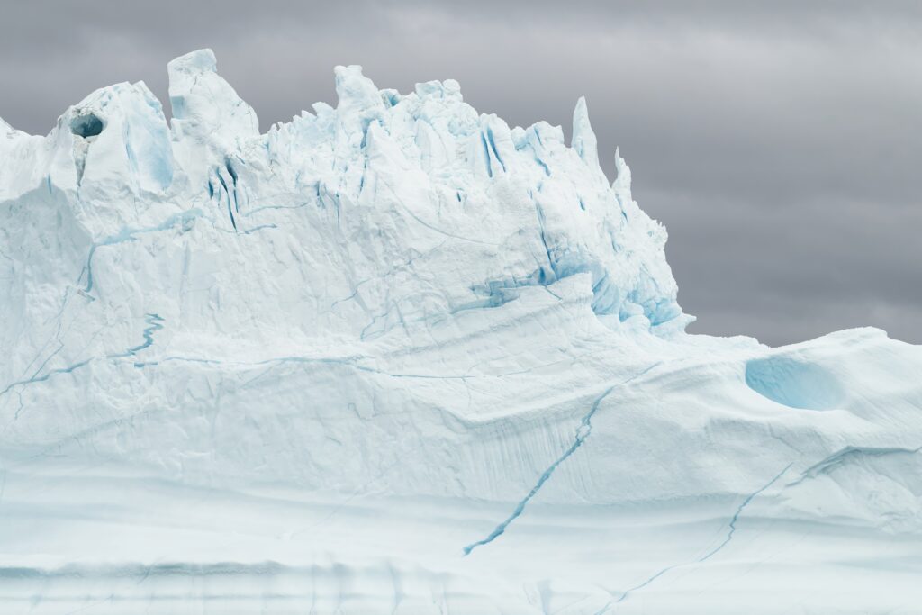 Jagged snow-covered rocks with ice formations under cloudy gray sky winter nature wallpaper background