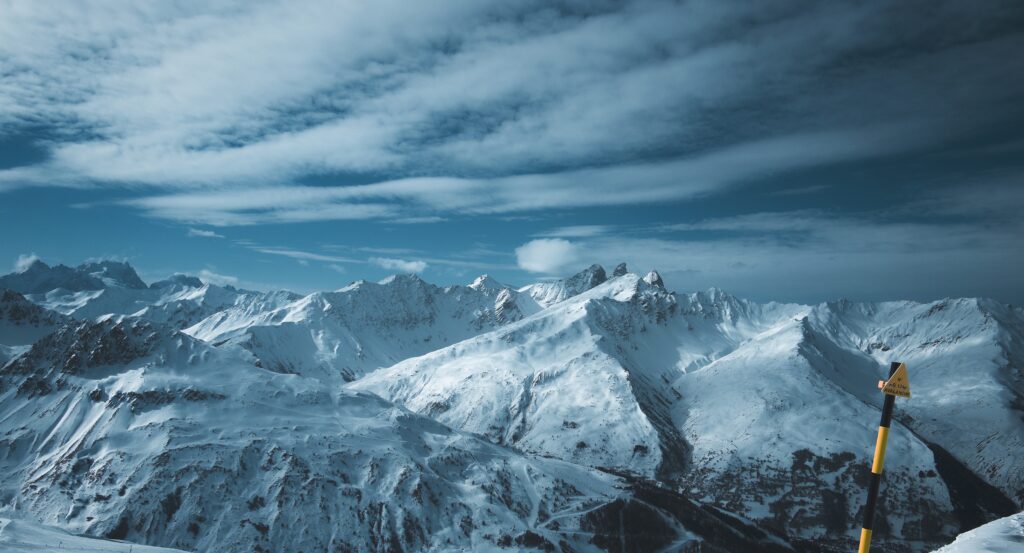 Snow-covered high mountains under dramatic sky with blue tones and sweeping clouds wallpaper