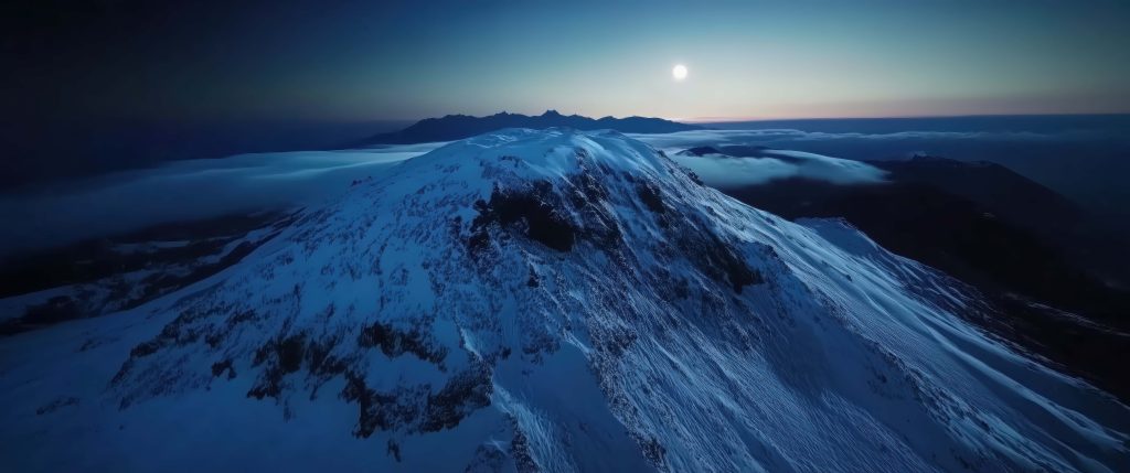 Snow-covered mountain peak above dense fog glowing blue twilight horizon landscape wallpaper