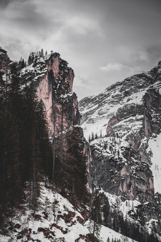 Snow-dusted rocky cliffs surrounded by dense evergreens create a serene winter landscape wallpaper