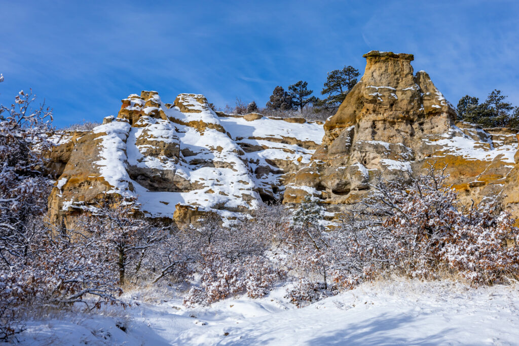 Rugged snow-covered rock formation with leafless trees under bright blue winter sky wallpaper background