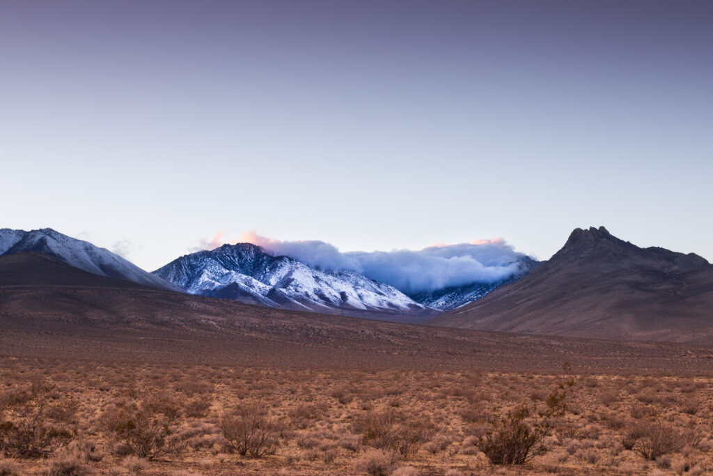 Vast desert landscape with snow-capped rugged mountains under serene gradient sky wallpaper
