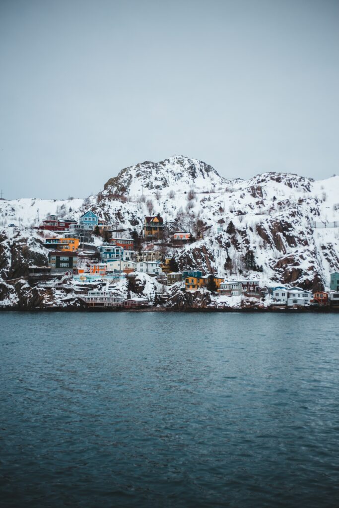 Colorful houses on snowy cliff by calm blue sea with rugged mountains and overcast sky wallpaper