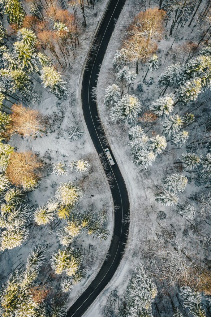 Aerial view of winding snowy forest road with single car and snow-dusted evergreen trees winter wallpaper