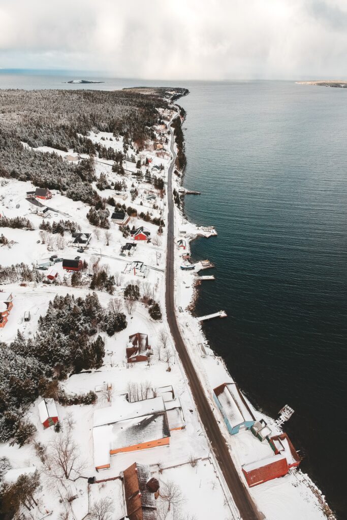 Aerial view of snowy island coast with scattered houses and winding road by calm blue sea Wallpaper