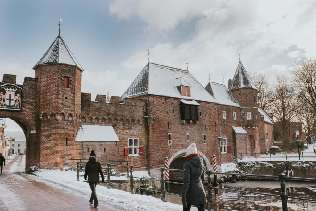 Historic medieval gate of Amersfoort covered in winter snow with people walking icy paths Wallpaper
