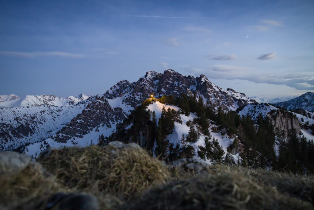 Snowy mountain peaks and evergreen trees under twilight sky with glowing cabin light wallpaper