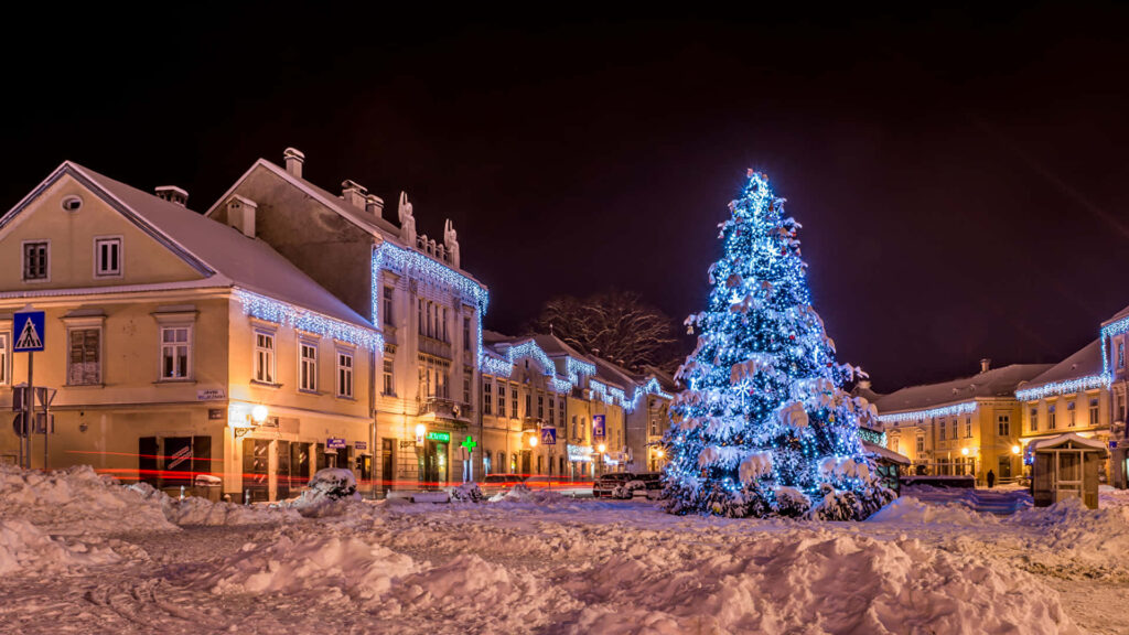 Enchanting Snowy Town Square at Night with Christmas Tree Wallpaper