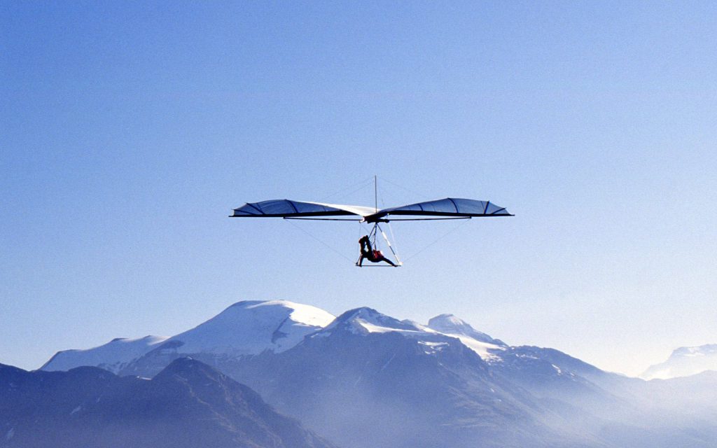 Hang glider soaring over snow-capped European Alps under bright blue sky wide-angle wallpaper