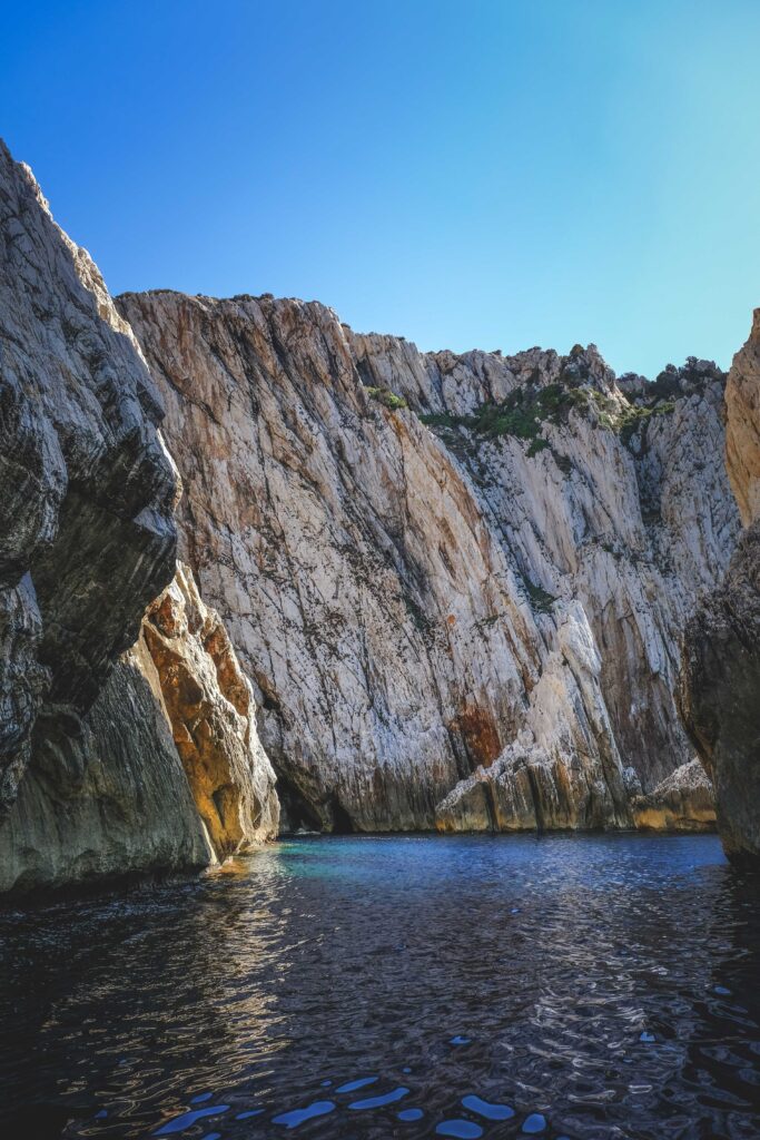 Soaring rocky cliffs and rugged mountains reflect on deep blue lake beneath clear vibrant sky wallpaper