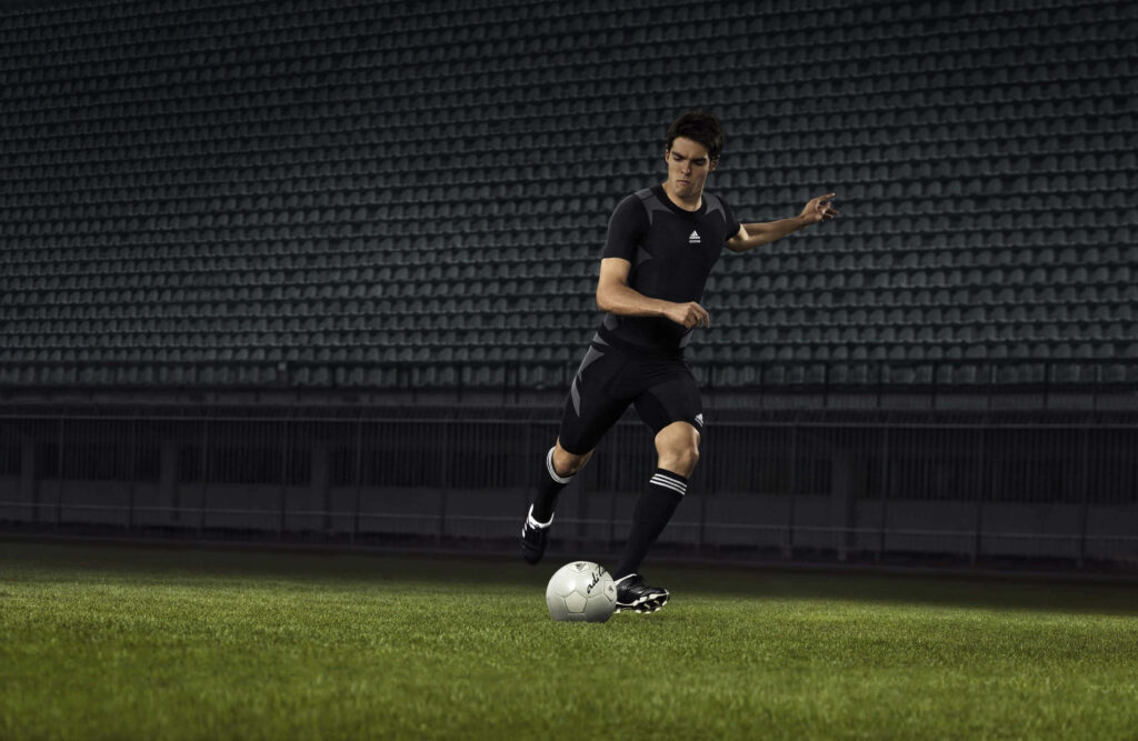 Dynamic Soccer Player Dribbling on Green Field - Wallpaper Background