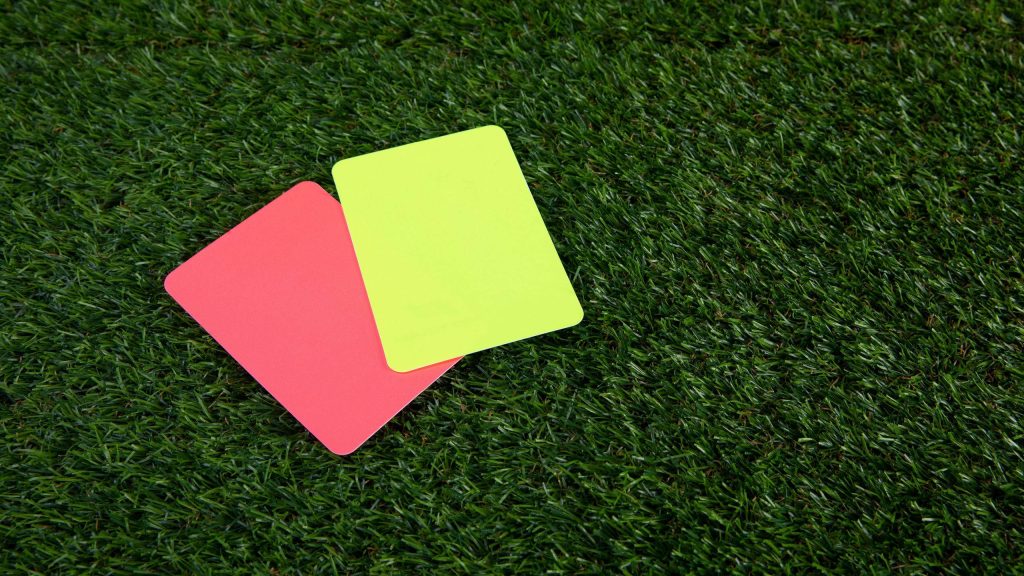 High-angle photo of red and yellow soccer cards on green artificial turf referee wallpaper background