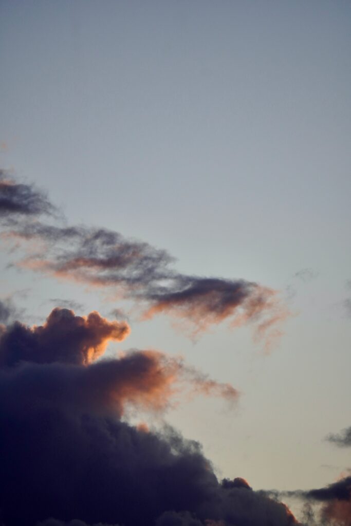 Dusk light filters through dramatic clouds over a serene twilight sky with soft blue and warm tones Wallpaper