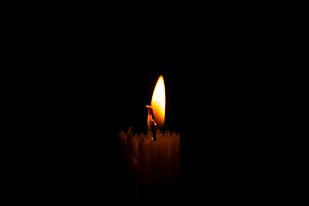 Single lit candle glowing softly with warm flame on dark minimalist background for calm ambiance Wallpaper