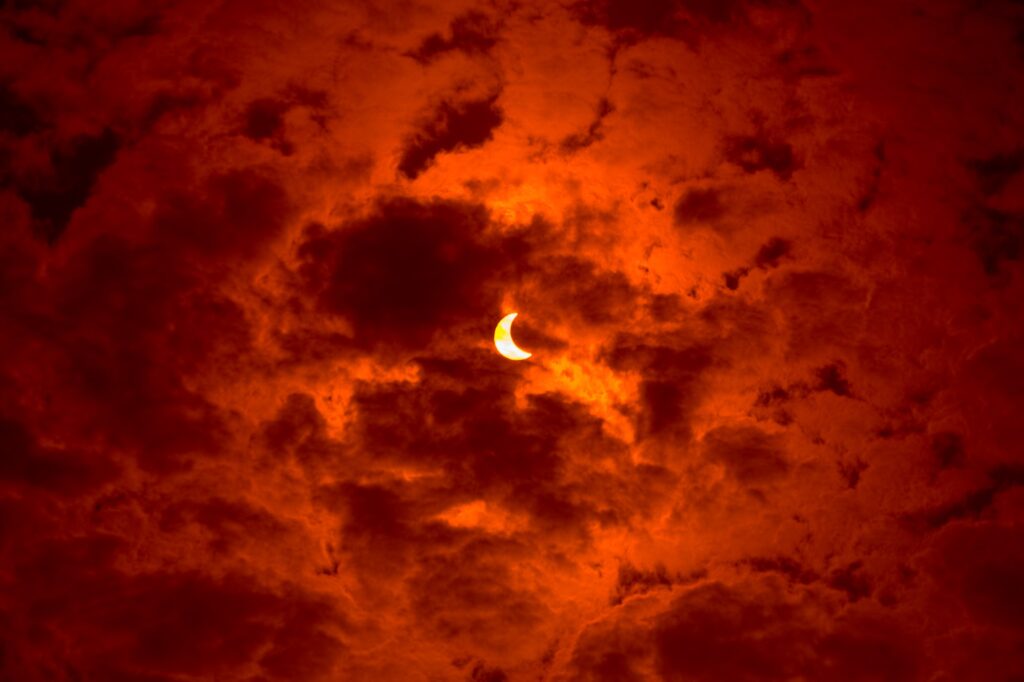 Solar eclipse with moon partially covering sun against vivid orange textured cloud sky wallpaper