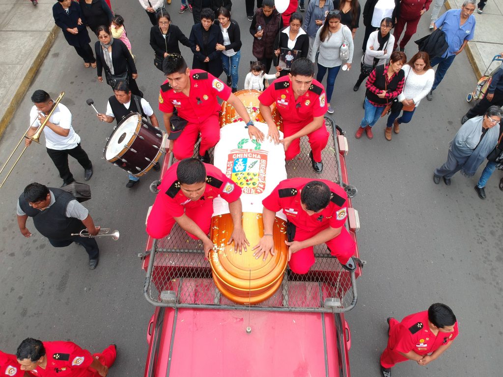 Funeral procession in Chincha Peru firefighters in red uniforms carrying coffin with civic crest Wallpaper