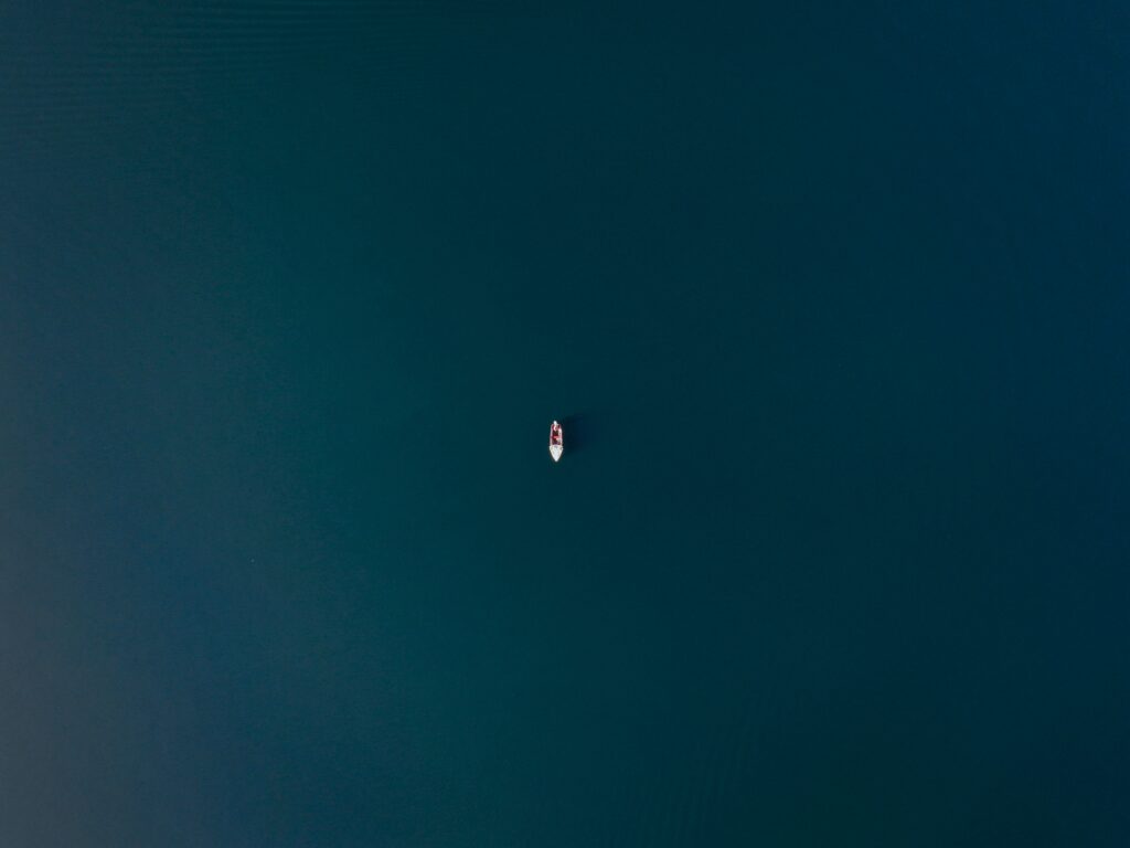 Aerial view of solitary boat on calm deep blue water with subtle ripples minimalist wallpaper background
