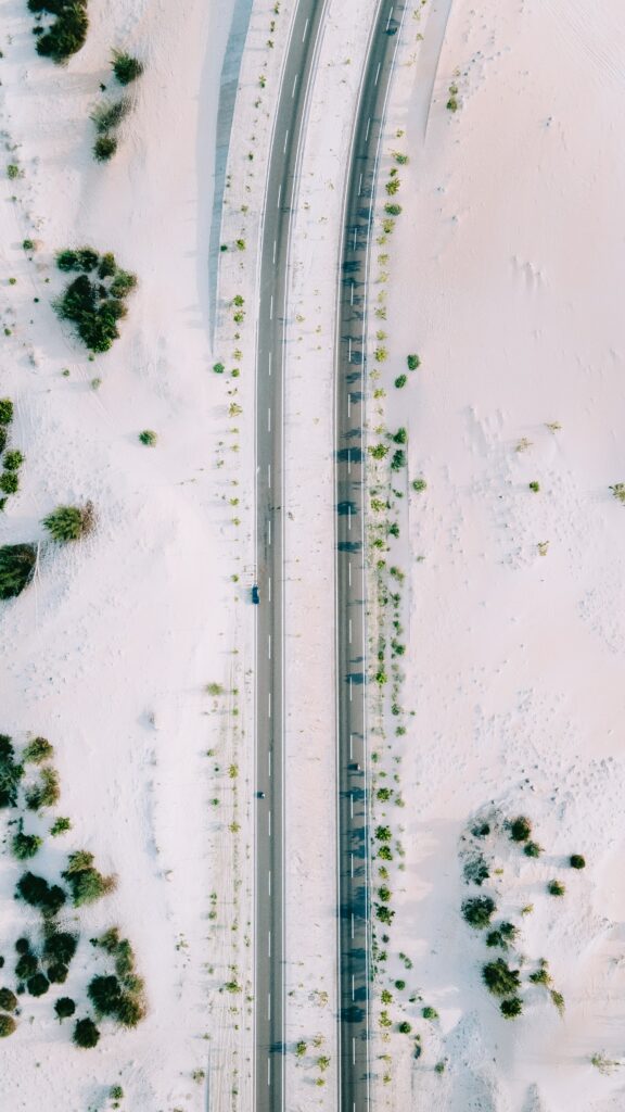 Aerial view of a car on a straight road through sandy terrain with green bushes minimalist wallpaper