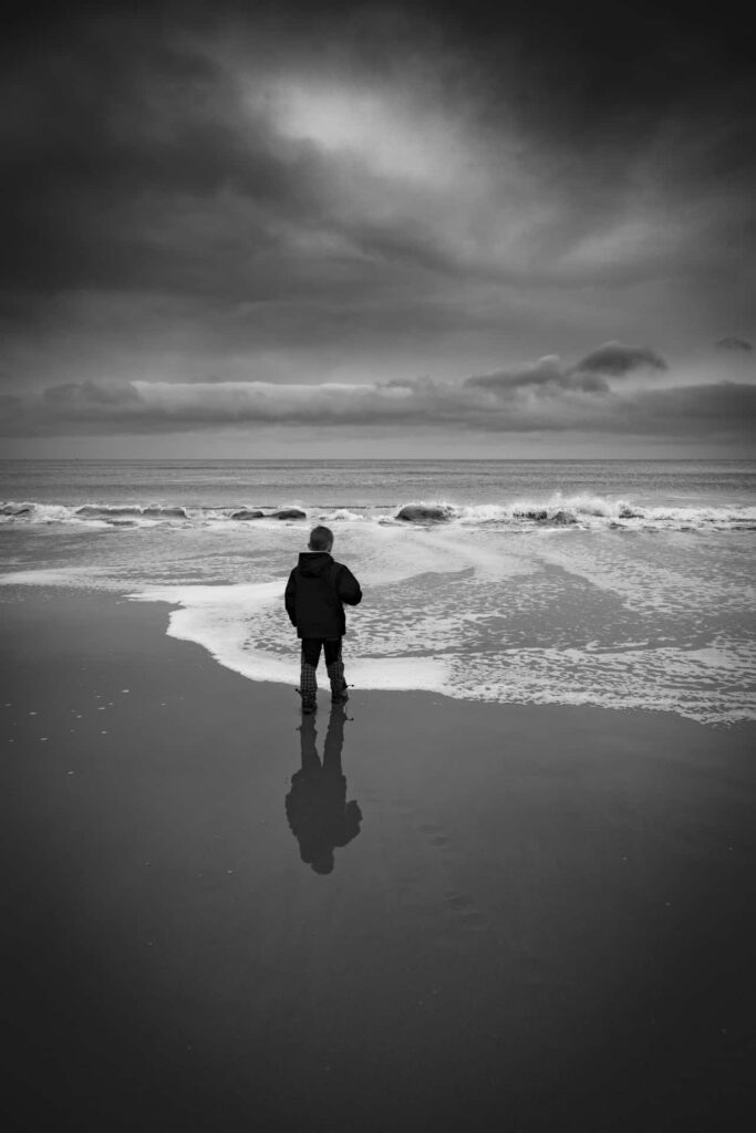 Solitary Figure on Beach: Serene Waves & Monochrome Sky Wallpaper