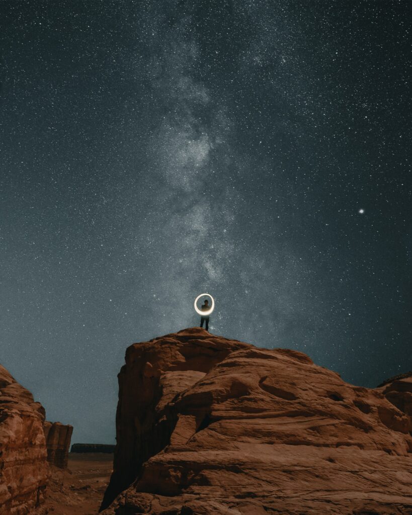 Solitary figure on canyon rocks under starry night sky with glowing Milky Way and serene isolation Wallpaper