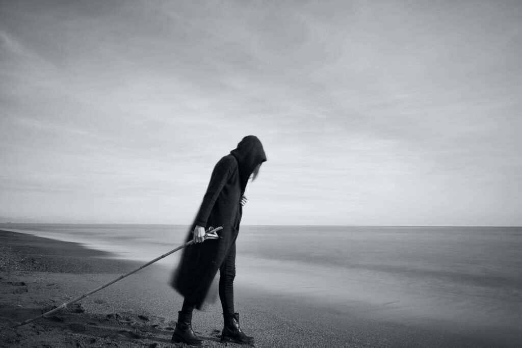 Solitary Figure on Desolate Beach: Introspection Under Overcast Sky Wallpaper