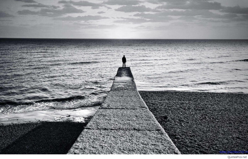 Grayscale Solitude: A Figure on a Pier by the Calm Ocean Wallpaper