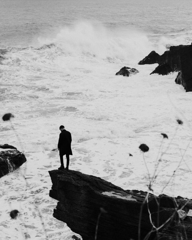 Solitary Figure Gazing at Tumultuous Sea - Dramatic Black & White Photo Wallpaper