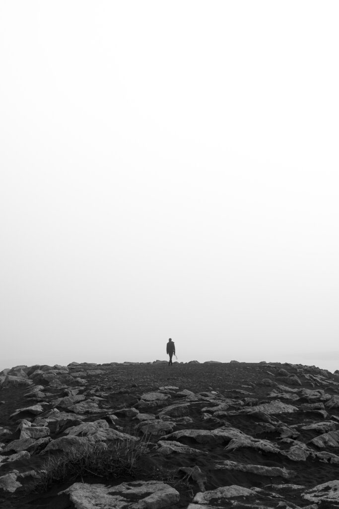 Solitary Figure on Rugged Rocks: Black and White Wallpaper Background