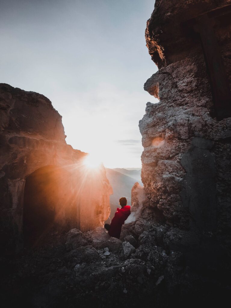 Solitary person on rugged rocks in golden sunlight reflecting serenity and quiet loneliness Wallpaper