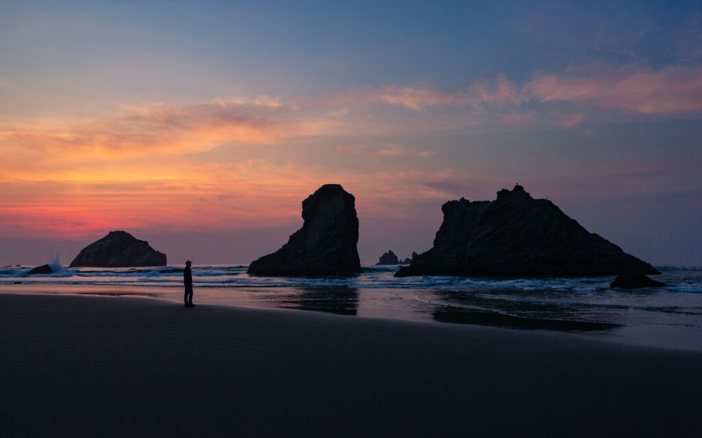 Solitary person on peaceful beach with dramatic rock formations and vibrant sunset sky wallpaper