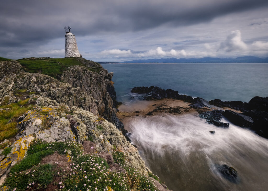 Solitary lighthouse on rugged cliff with rocky shores and dramatic cloudy sky coastal landscape Wallpaper