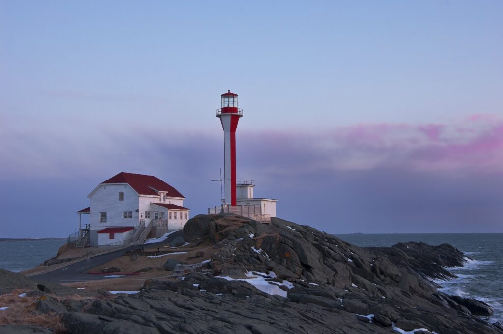 Solitary lighthouse with red roof on rugged rocks by sea under purple blue tranquil sky wallpaper