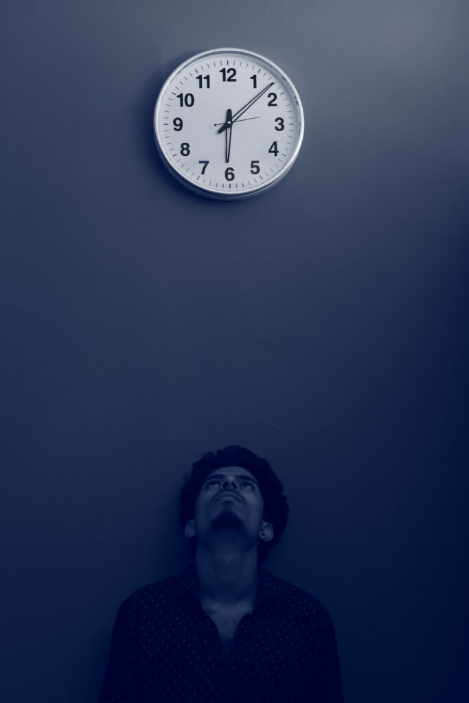 Solitary man gazing at round wall clock minimalist deep blue background time contemplation wallpaper