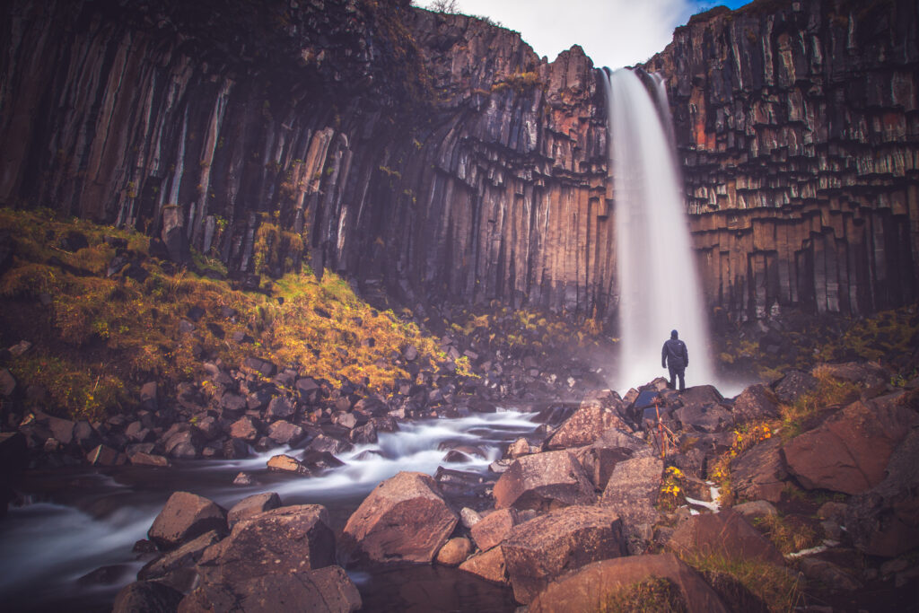 Silhouette of man by waterfall cascading over rock columns with moss and rugged stones background Wallpaper