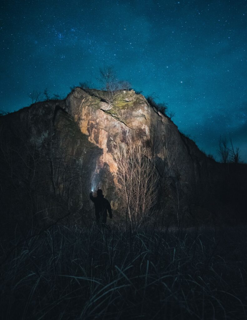 Solitary man silhouette shining light on rugged rock under starry night sky wallpaper background
