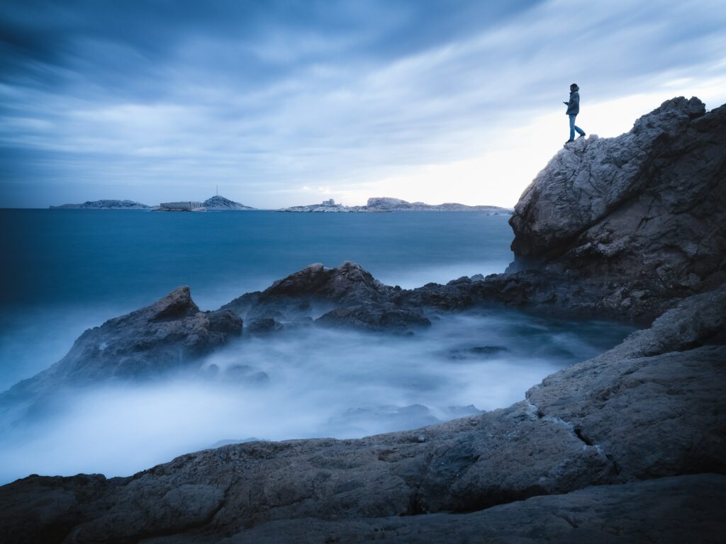Solitary man on rugged cliff overlooking misty blue sea with dramatic clouds serene mood wallpaper