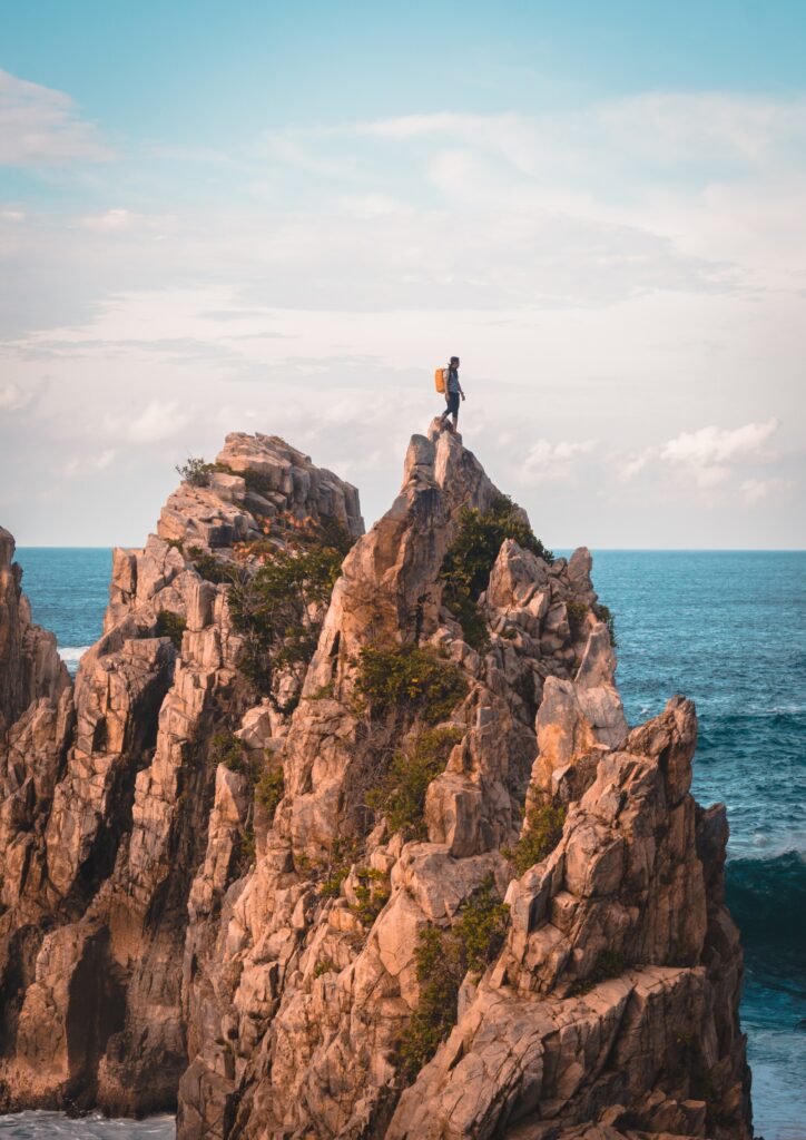 Man on rugged rock overlooking vast blue ocean coastal Indonesia adventure solitude wallpaper