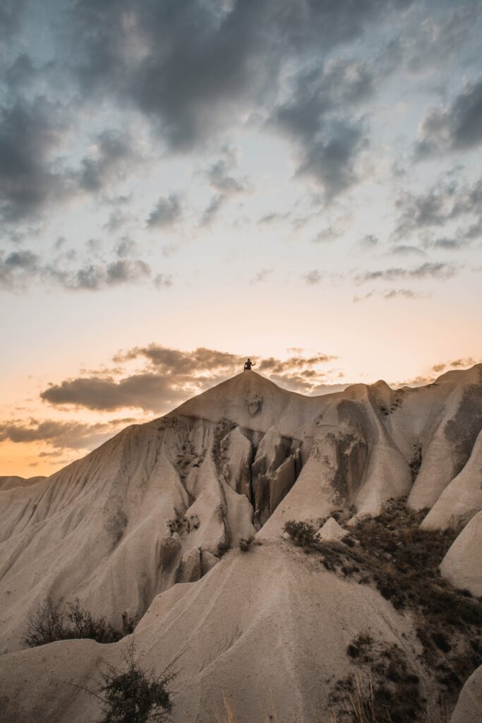 Silhouette of lone man on rugged mountain peak with sandy rocks under warm sunset sky wallpaper