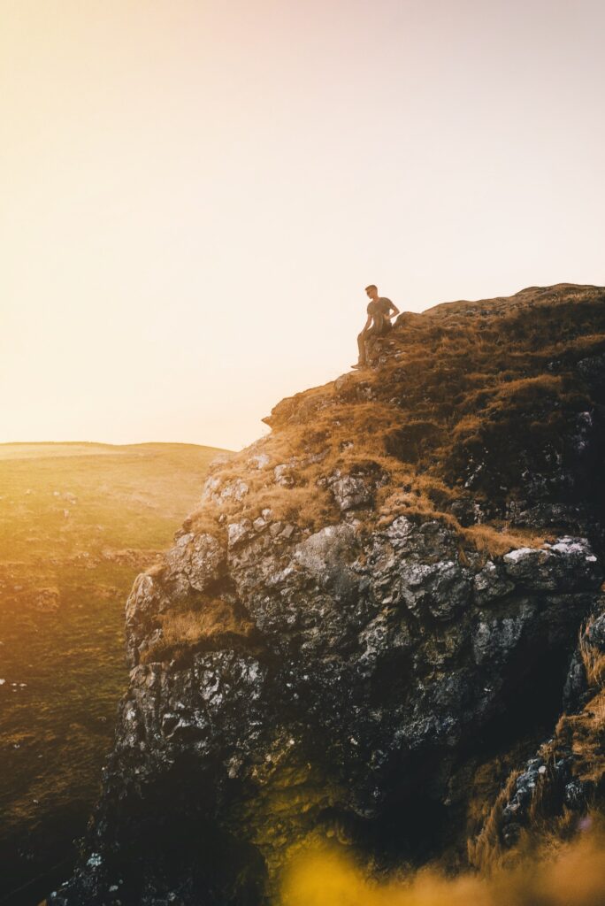 Solitary man on rugged Peak District mountain cliff bathed in warm golden sunlight serene view Wallpaper