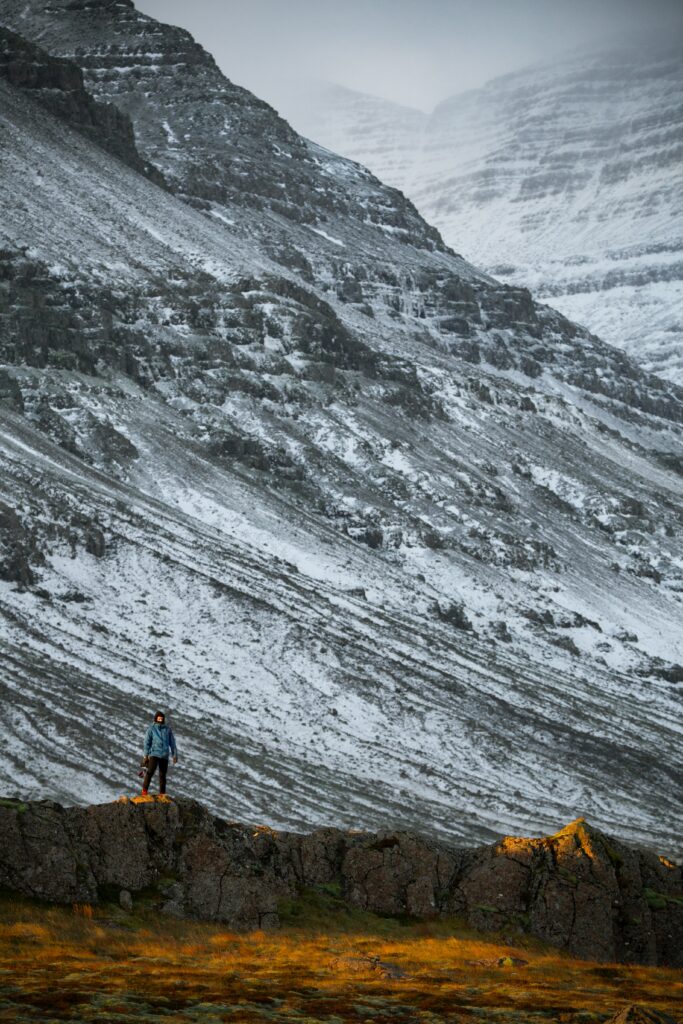 Man standing on rugged rocks overlooking snow dusted mountains nature landscape wallpaper background