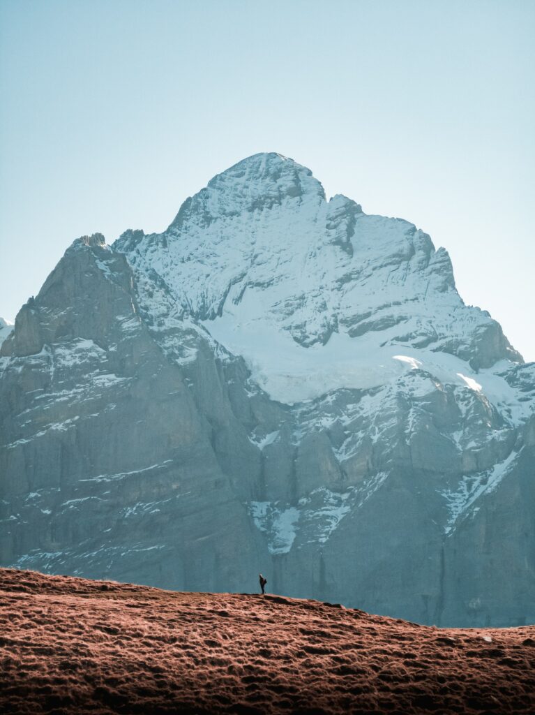 Solitary man on rugged slope below snow-capped peak in serene untouched mountain landscape Wallpaper