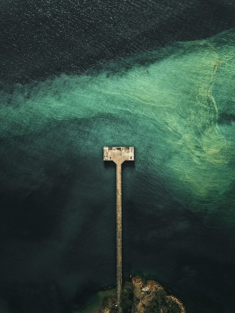 Aerial view of solitary pier over deep blue and turquoise textured sea with gentle waves wallpaper