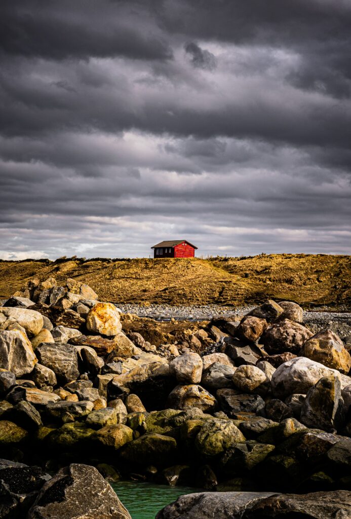 Solitary red house on rugged hilltop with golden grass and dramatic cloudy sky background Wallpaper
