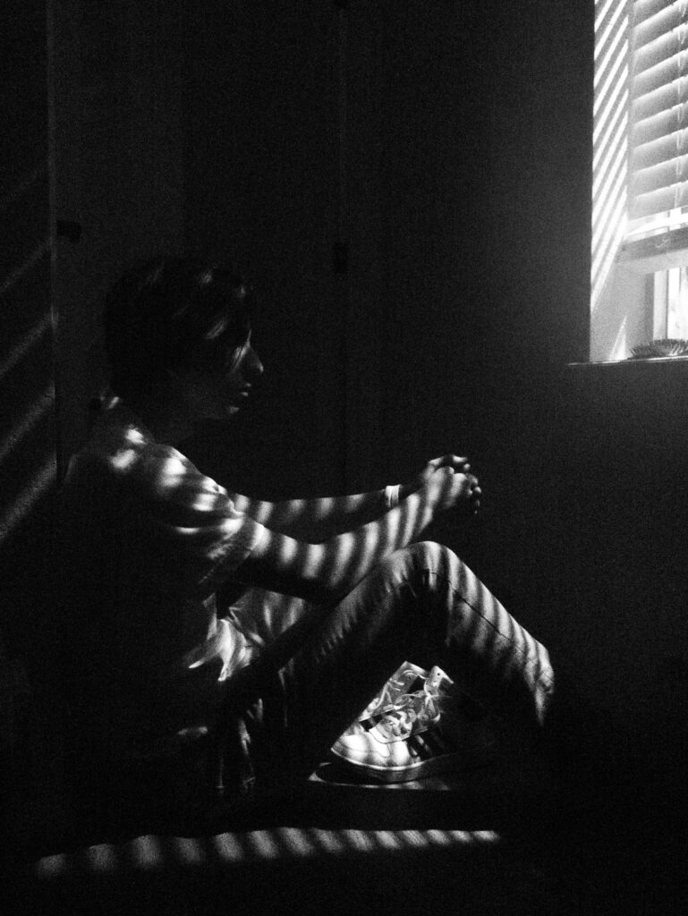 Solitude: A glimpse into the melancholic world of a young boy, lost in thoughts, seeking solace indoors amidst sun-kissed rays Wallpaper