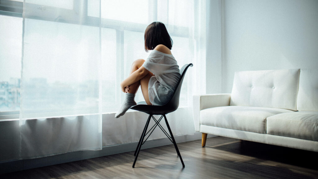 Woman with short hair curled on black chair sunlit window minimalist serene 4K wallpaper background
