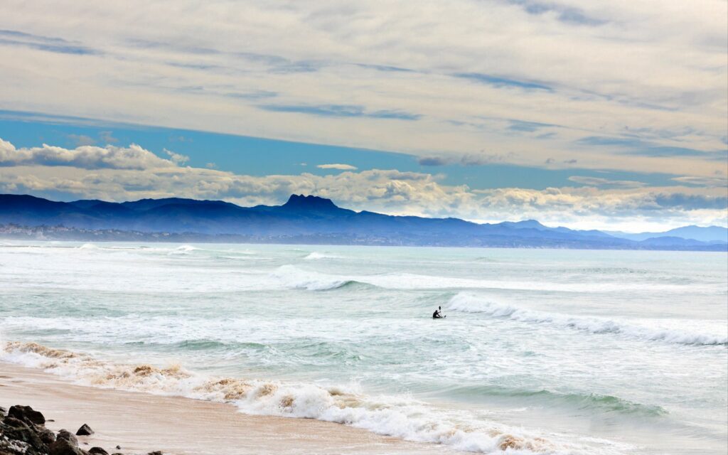Serene ocean wallpaper with lone rower near sandy coast mountains dramatic sky clouds