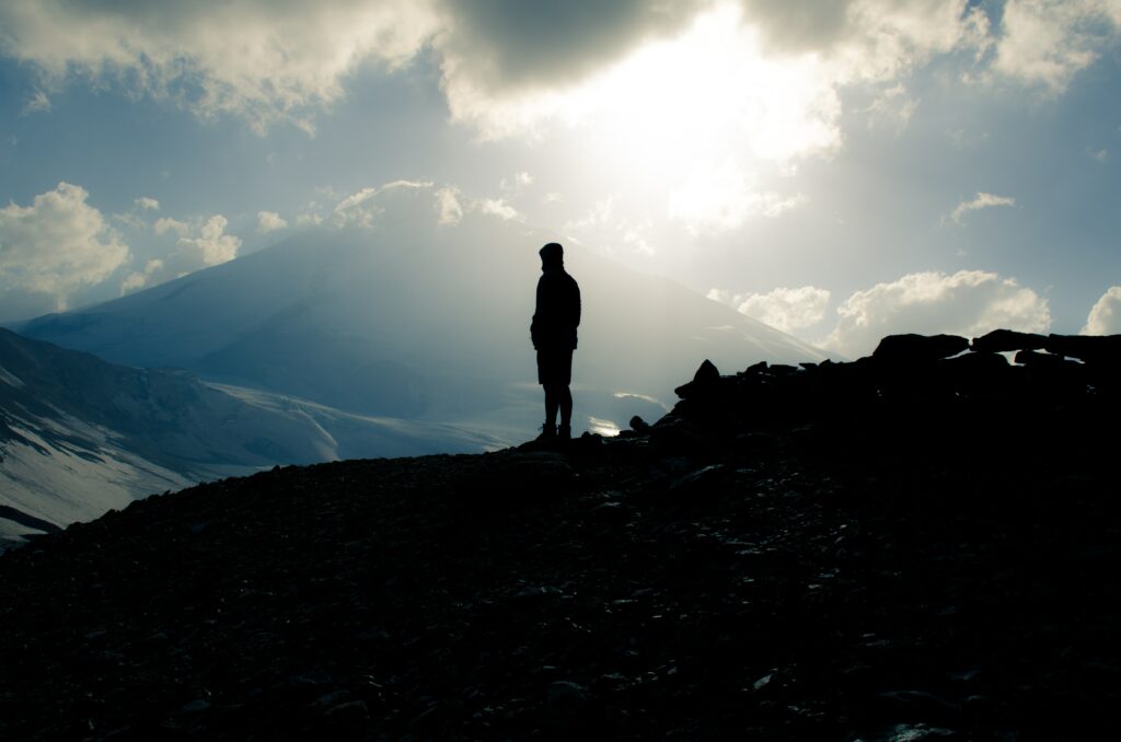 Silhouette of lone figure on Mount Elbrus Russia with sunlit clouds and rugged mountain landscape Wallpaper